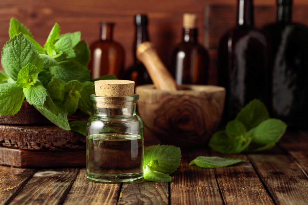 A small jar of peppermint oil and some fresh mint leaves on a wooden table