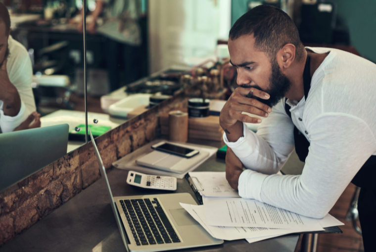 Barbershop owner studies his laptop as he calculates his taxes